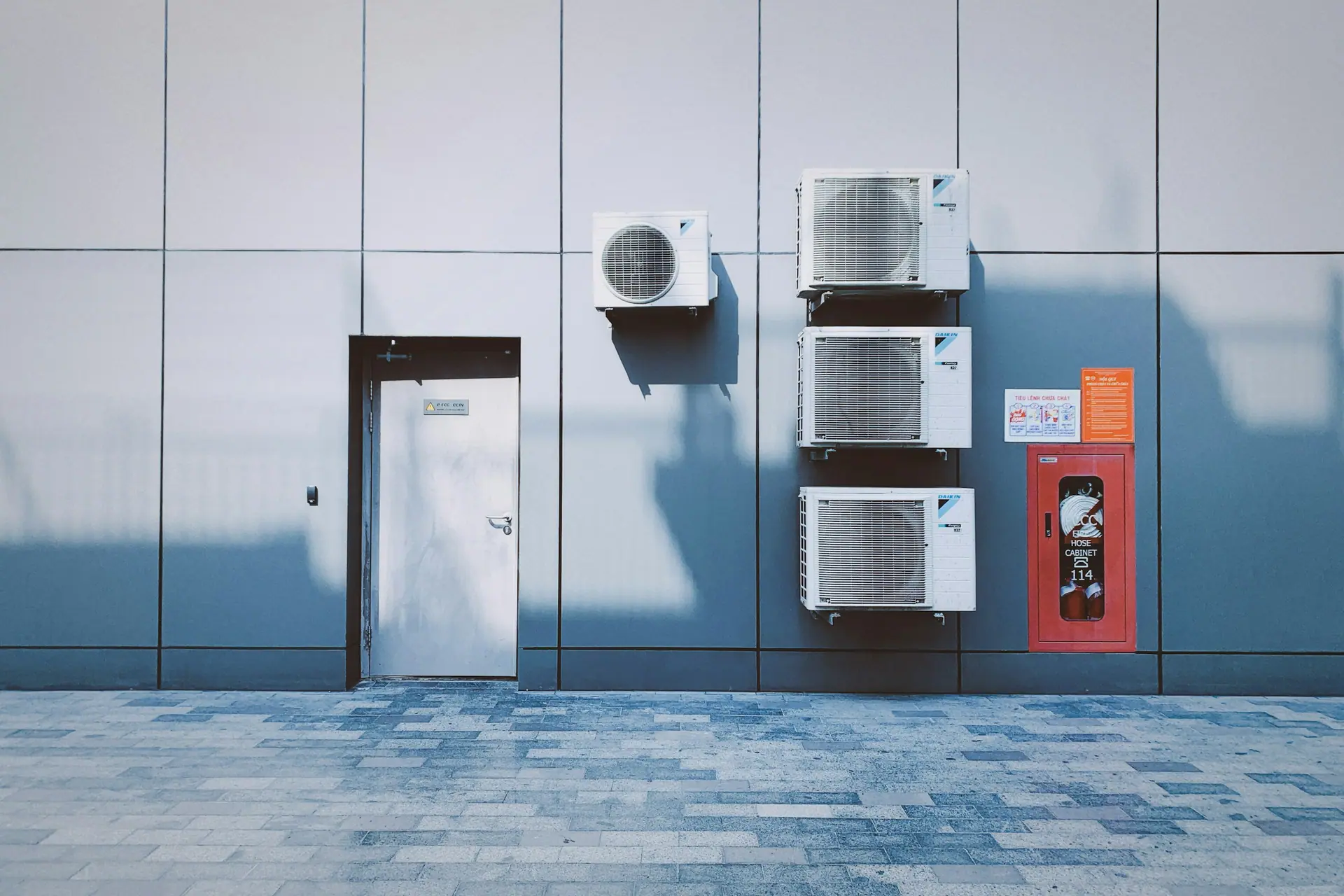 Wall-mounted outdoor air conditioning units on a grey panelled building